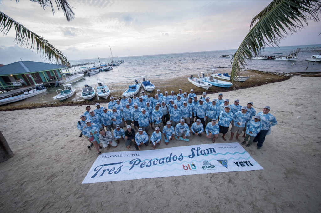 Group of people in blue-and-white shirts and caps posing near a tarpaulin about the Tres Pescados Slam Tourney